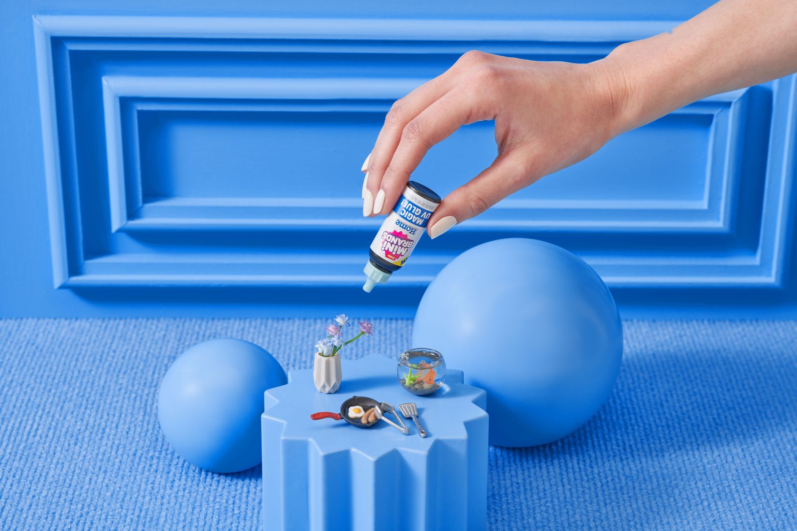 A hand placing a tiny Mini Brands bottle on a blue podium